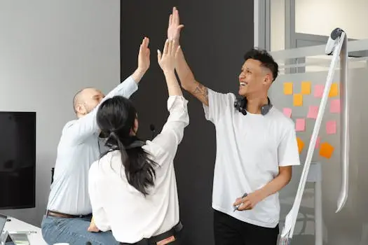 Diverse team members in an office high-fiving, symbolizing success and teamwork in a supportive environment.